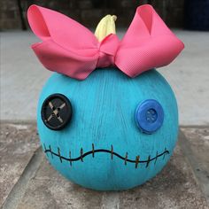 a blue pumpkin with a pink bow on it's head sitting on the ground