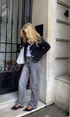 a woman standing on the steps of a building with her hands in her pockets and looking down