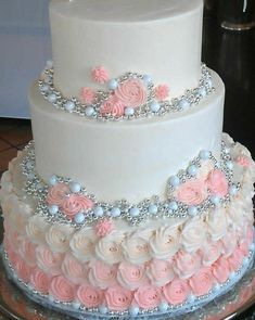 a three tiered wedding cake with pink and white frosting roses on the side