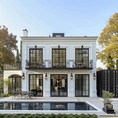 a white house with black windows and balconies on the second floor is surrounded by greenery