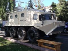 an armored vehicle is parked on the side of the road in front of a park bench