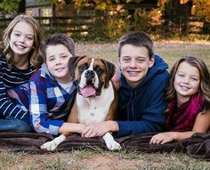 a family poses with their dog on a blanket in front of some trees and grass