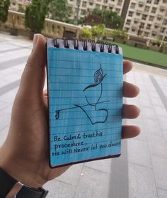 a hand holding up a notebook with writing on it in front of a large building