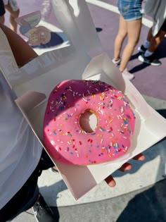 a pink donut with sprinkles in a box on the street while people walk by