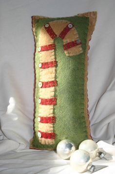 a green pillow with red and white trim on it next to christmas ornaments in the shape of a candy cane