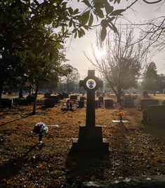 the sun shines through the trees over an old cemetery with headstones and flowers