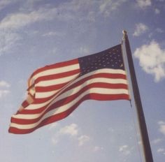 an american flag waving in the wind on a clear day with blue sky and clouds