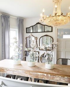 a dining room table with vases and flowers on it in front of a mirror