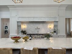 a large kitchen with marble counter tops and white cabinets, along with two gold bowls filled with fruit