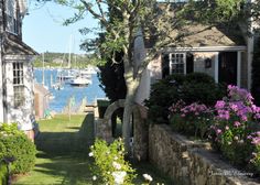 there is a house with flowers in the front yard and boats on the water behind it