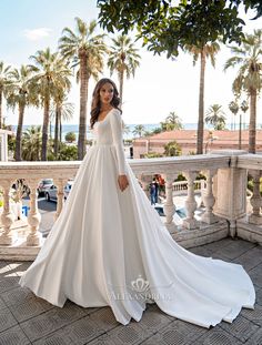 a woman in a white wedding dress standing on a balcony with palm trees behind her