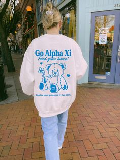 a woman is walking down the street with a teddy bear on her back and go aloha xi t - shirt