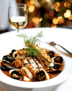 a white plate topped with seafood and mussels next to a glass of wine