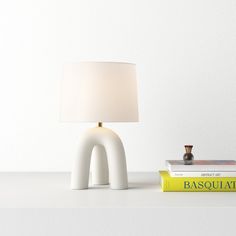 a lamp sitting on top of a white table next to two books and a small figurine