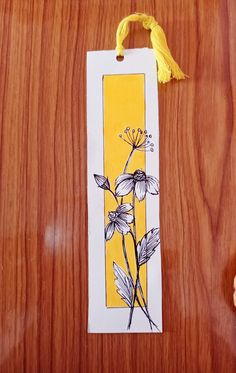 a bookmark with flowers on it sitting on top of a wooden table next to an orange flower