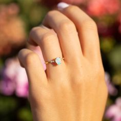 a woman's hand with a ring on it and pink flowers in the background