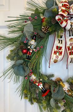 a christmas wreath hanging on the front door with ornaments and greenery around it's edges