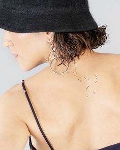 the back of a woman's neck with small stars on her left shoulder and large hoop earrings