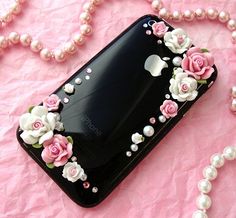 an iphone case with pink roses and pearls on it sitting on a pink surface next to a pearl necklace