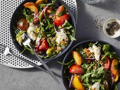 two black bowls filled with salad on top of a gray table next to silver spoons