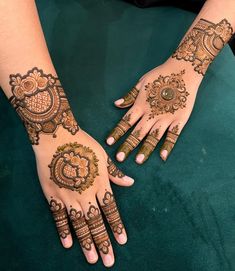 two hands with henna designs on them sitting on a green cloth covered table top