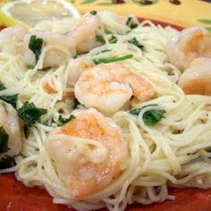 pasta with shrimp and spinach is on a red plate next to lemon wedges