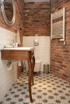 a bathroom with a sink, toilet and brick wall behind the shower area is shown