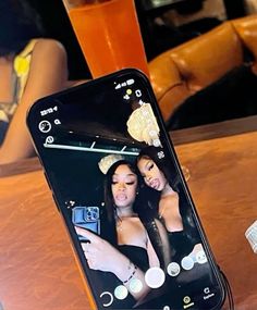 a cell phone with an image of two women on it sitting on a table next to a drink