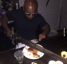 a man cutting up food on top of a table next to a knife and glasses