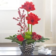 a vase with red flowers and greenery on a table