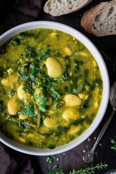 a white bowl filled with green soup next to slices of bread and sprigs of parsley