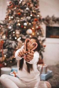 a woman holding up a candy cane in front of a christmas tree