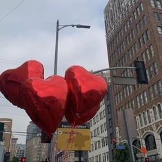 two red heart shaped balloons floating in the air on a city street with tall buildings