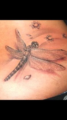 a woman's stomach with a dragonfly tattoo on the side and flowers around it