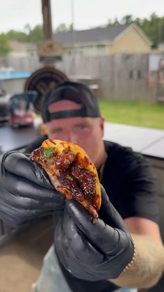 a man in black gloves holding up a slice of pizza