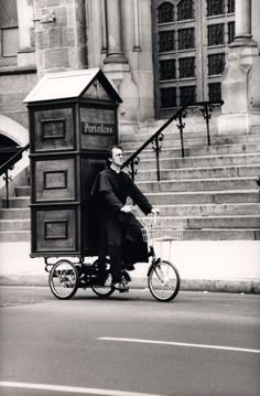 an old photo of a man riding a bike with a phone booth on the back