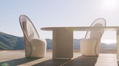 two chairs and a table sitting on a wooden deck with mountains in the back ground