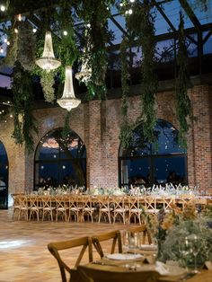 an indoor venue with tables and chandeliers hanging from the ceiling, surrounded by greenery