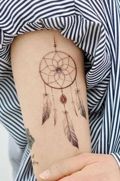 a woman's arm with a tattoo that has a small dream catcher on it