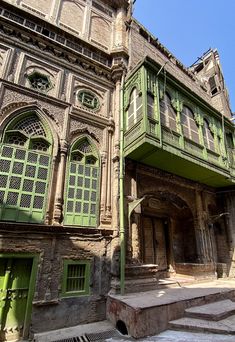 an old building with green doors and windows on the outside, surrounded by stone steps