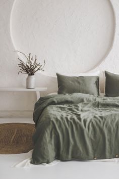 a bed with green sheets and pillows in front of a round wall hanging above it