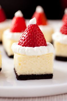 small cheesecakes decorated with strawberries and whipped cream are on a white plate