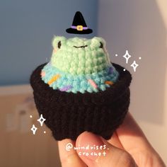 a hand holding a small crocheted cupcake with a witches hat on top