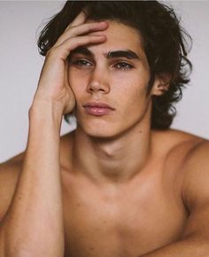 a shirtless young man holding his hand to his face while looking at the camera