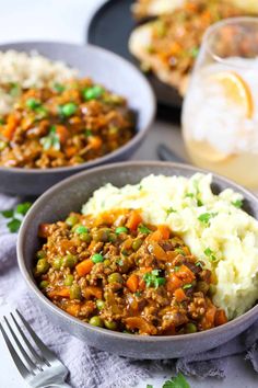 two bowls filled with mashed potatoes, meat and veggies next to a glass of wine