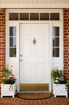 two white planters with flowers are on the front steps of a brick house,