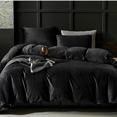 a bed with black sheets and pillows on top of it in front of a wall