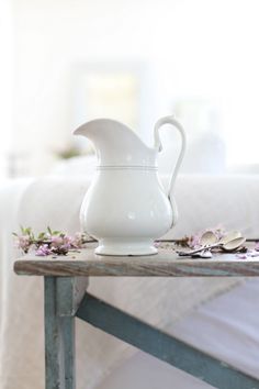 a white pitcher sitting on top of a wooden table next to a flowered bed