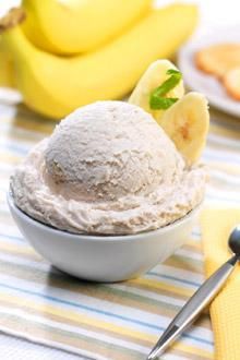 a bowl filled with ice cream next to bananas and spoons on a tablecloth