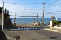 an empty street next to the ocean with power lines above it and telephone poles on either side